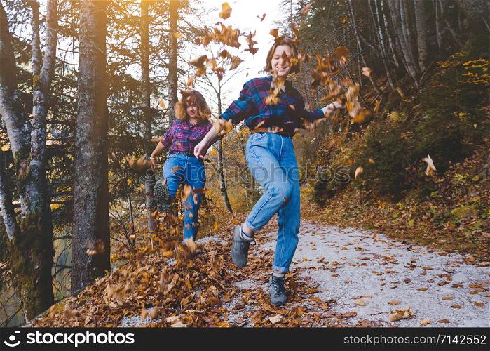 autumn fun. Two happy girls in the forest throw dry leaves