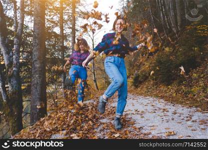 autumn fun. Two happy girls in the forest throw dry leaves