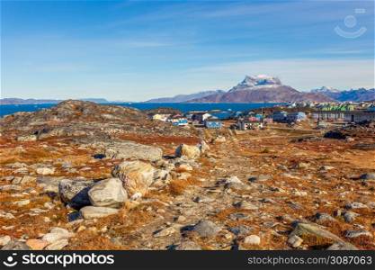 Autumn greenlandic tundra with orange grass, stones, Inuit settlement and Sermitsiaq mountain in the background, Nuuk, Greenland