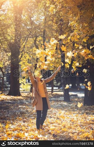 autumn. happy smiling girl outdoors throw yellow maple leaves