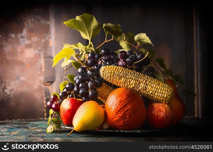 Autumn harvest concept. Plate with fall fruits and vegetables on dark rustic kitchen table at wooden background, side view, place for text