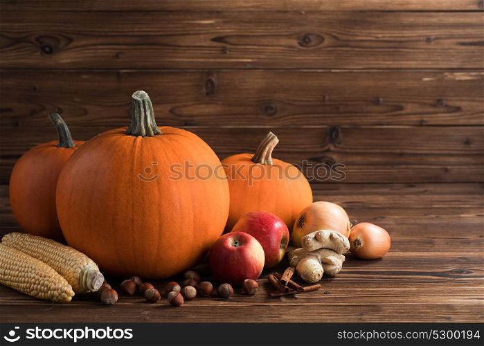 Autumn harvest on wooden table. Autumn harvest still life with pumpkins, apples, hazelnut, corn, ginger, onion and cinnamon on wooden background
