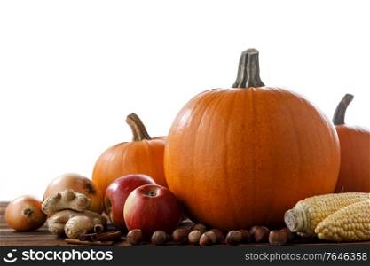 Autumn harvest still life with pumpkins, apples, hazelnut, corn, ginger, onion and cinnamon on wooden table isolated on white background. Autumn harvest on wooden table