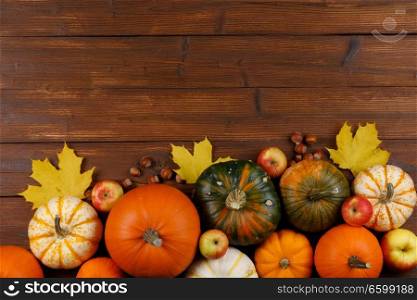 Autumn harvest still life with pumpkins , apples , hazelnuts and dry maple leaves on wooden background , top view. Autumn harvest on wooden table
