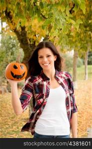 Autumn has arrived. Pretty brunette in a park with a Halloween pumpkin