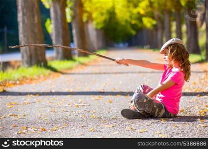autumn kid girl with camouflage pants pointing with hiker branch stick