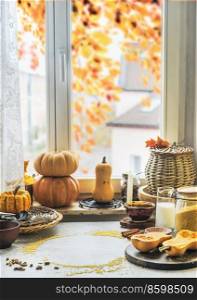 Autumn kitchen still life with various pumpkins, kitchen utensils and ingredients at concrete table with window background with fall foliage. Seasonal cooking at home. Front view.