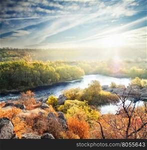 Autumn landscape with a mountain river and trees under a bright sun. Autumn landscape with a mountain river