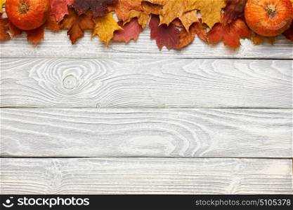 Autumn leaves and pumpkins over old wooden background with copy space