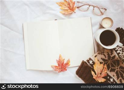 Autumn lifestyle concept, blank notebook and eyeglasses with knitted hat on white bed sheet background
