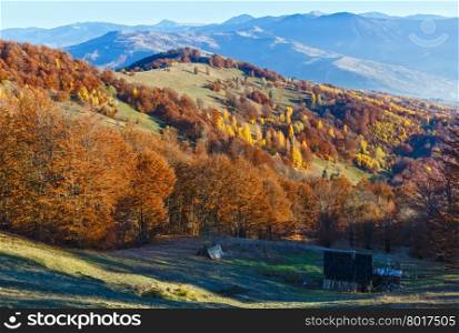 Autumn misty mountain landscape with colorful trees on slope and wooden barn in front.