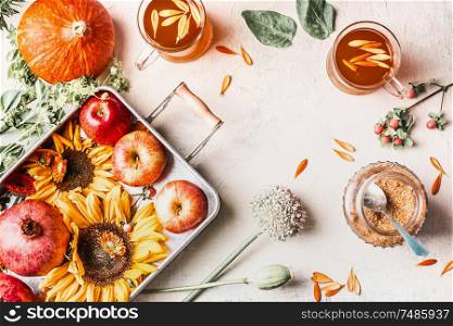 Autumn or late summer composition with sunflowers, pumpkin, apples, flowers and herbal tea in glass cups on white desktop. Top view. Copy space. Frame