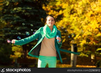 Autumn outdoor relaxation and recreation concept. Woman walking in park making soap bubble having fun during autumnal weather.. Woman walking in park making soap bubble
