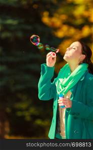 Autumn outdoor relaxation and recreation concept. Woman walking in park making soap bubble having fun during autumnal weather.. Woman walking in park making soap bubble