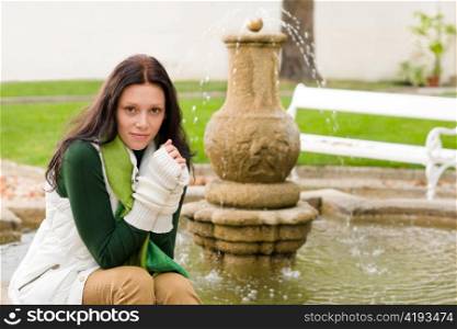 Autumn park young beautiful woman sitting on fountain cloudy day