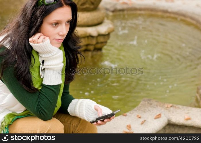 Autumn park young woman dialing phone sitting on fountain