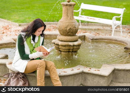 Autumn park young woman reading book sitting on fountain