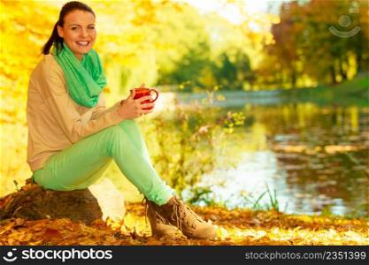 Autumn picnic concept. Woman relaxing in park or autumnal forest drinking hot warming drink from mug.. Woman relaxing in park drinking drink from mug