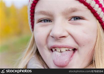 Autumn portrait of blond girl in sunlight puts out tongue