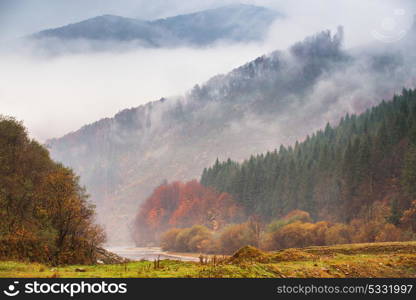 Autumn rain and fog in the mountains. Fog over the river. Thick fog around highest mountain tops. Colorful autumn forest background