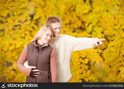 Autumn romantic couple happy together hugging in park pointing