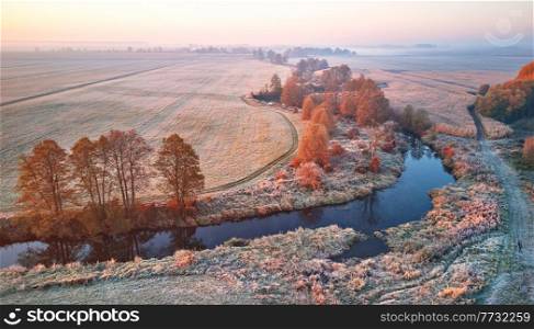 Autumn rural landscape. Frost on grass. River, field, meadow, village, fall color trees. Sunrise morning aerial panorama. Belarus