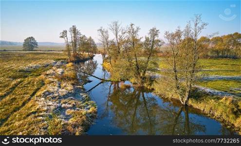 Autumn rural landscape. Frost on grass. River, green field, meadow, trees on riverbank. Dirt road on grassland. Sunrise fall morning aerial panorama. Belarus