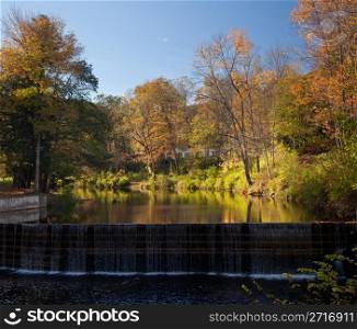 Autumn scene in Vermont as leaves are reflected in calm river by old fashioned dam