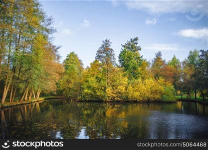 Autumn scenery with a small lake surrounded by trees in autumn colors with tree reflections in the water and autumn leaves