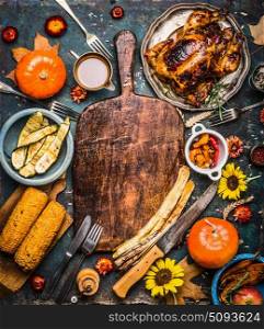 Autumn seasonal cooking and eating background with cutting board, roasted organic harvest vegetables , pumpkin, whole turkey or chicken and fall flowers , top view. Thanksgiving dinner background