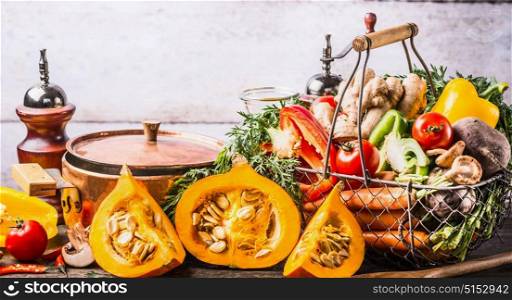 Autumn seasonal cooking concept. Various autumn seasonal organic vegetables: pumpkin,carrot,paprika,ginger in basket with cooking pot on wooden kitchen desk tables , front view.