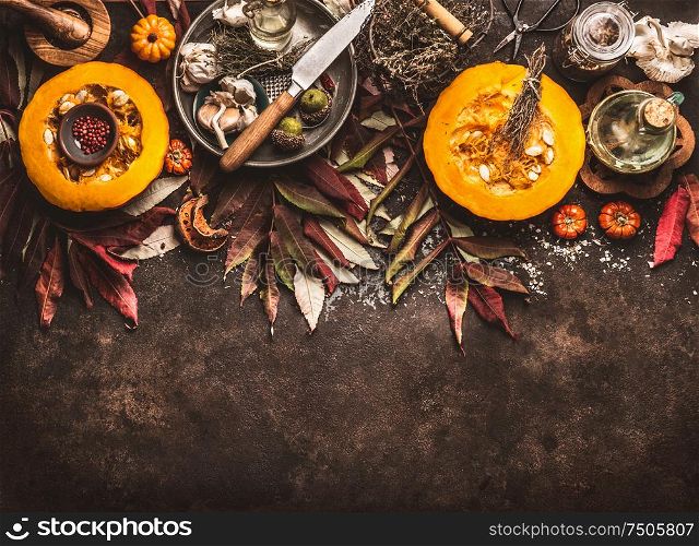 Autumn seasonal food background with halved pumpkin, knife , herbs and spices on dark rustic background with fall leaves. Top view. Border