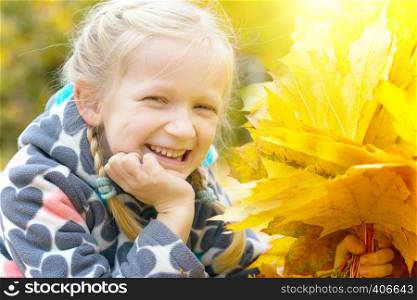autumn - smiling little girl with a maple leaf on the street