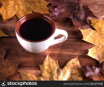 Autumn still life cup with tea on maple leaves on a wooden table. Cup with fruit tea and dry autumn leaves on a wooden background