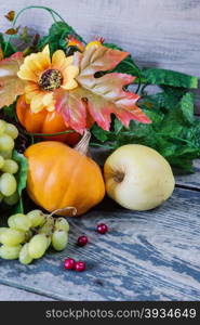 Autumn Still Life: green grapes in a basket and ripe apples, red cranberries, orange decorative pumpkin and squash with leaves on the wooden background