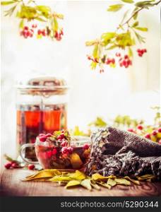 Autumn still life with cup and tea pot with red berries, scarf and fall leaves at sunny nature background