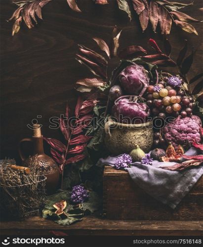 Autumn still life with purple fruits and vegetables on dark wooden table with fall leaves. Garden harvest. Organic farm production. Cozy home