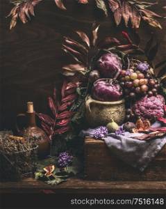 Autumn still life with purple fruits and vegetables on dark wooden table with fall leaves. Garden harvest. Organic farm production. Cozy home