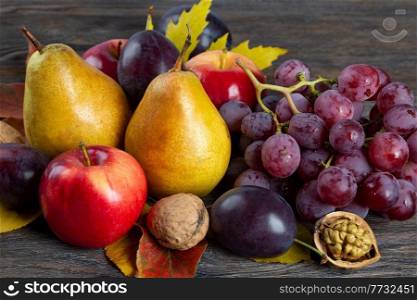 Autumn still life with walnuts, grape, pears and apple. Fruit and nuts on a brown wooden background