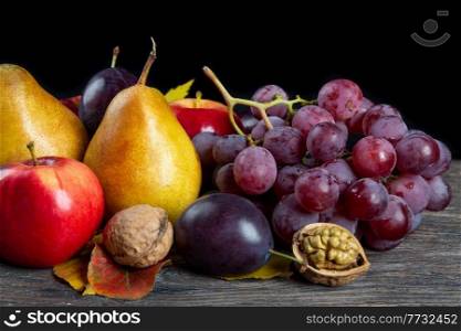 Autumn still life with walnuts, grape, pears and apple on a brown wooden table. Fruit and nuts on a black background