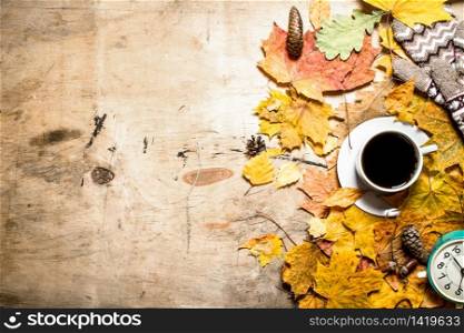 Autumn style . Cup of coffee with alarm clock on autumn leaves. On wooden background.. Cup of coffee with alarm clock on autumn leaves.