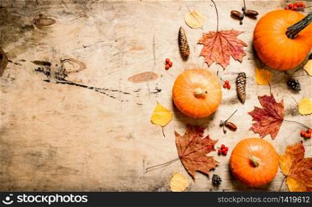 Autumn style. Pumpkin with autumn leaves and fir cones. On wooden background.. Pumpkin with autumn leaves and fir cones.