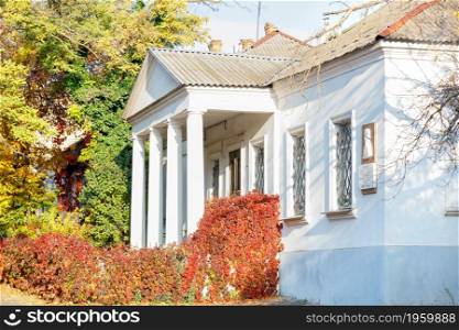 Autumn sunlight shines brightly on an old house with white columns and red wild grapes twisting along the facade of the building.. Colorful autumn landscape of an old house with white columns and bright red wild grapes on the facade with a sunny day.