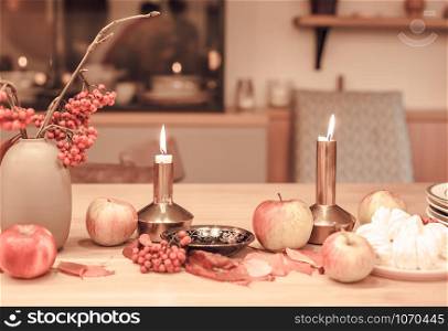 Autumn table decoration for Holiday Thanksgiving dinner. Cozy warm natural style with candles lights, red berries and apples