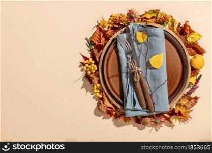 Autumn thanksgiving table place setting with cutlery, wooden plate and arrangement of fall leaves, copy space