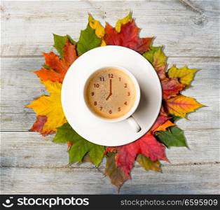 Autumn time. Coffee cup with clock symbol on fallen colorful leaves on wooden table, top view. Autumn coffee time