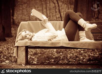 Autumn time education concept. Blonde girl with red book. Attractive woman sitting on the blanket in the park. . Blonde girl with red book.