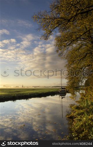 Autumn trees along a canal with a sailing boat seen from the castle estate in the Dutch village Warmond. Autumn trees along a canal