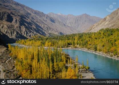 Autumn view of Ghizer river flowing through forest in Gahkuch, surrounded by Hindu Kush mountain range. Gilgit Baltistan, Pakistan.