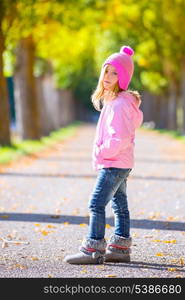 autumn winter kid girl blond with jeans and pink snow cap in trees track